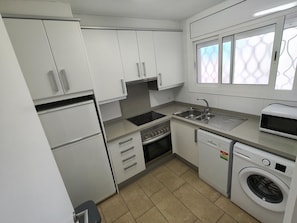 A compact kitchen with white cabinets, a built-in oven, a dishwasher, a microwave, and a washing machine.