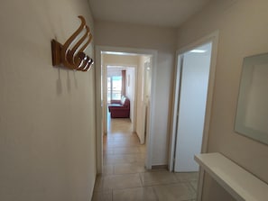 A hallway with a door leading to a room, a wall-mounted light fixture, and a tiled floor.