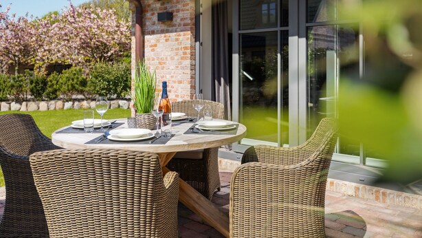 An outdoor dining area with wicker chairs and a round table set for two, featuring a bottle of wine and glasses. - House Munkmarscher Straße 14c (Westerland)