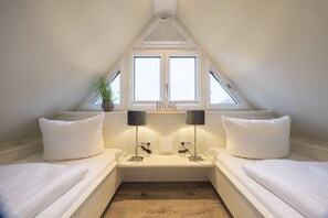 A bedroom with two beds, a window, a plant, and two lamps.
