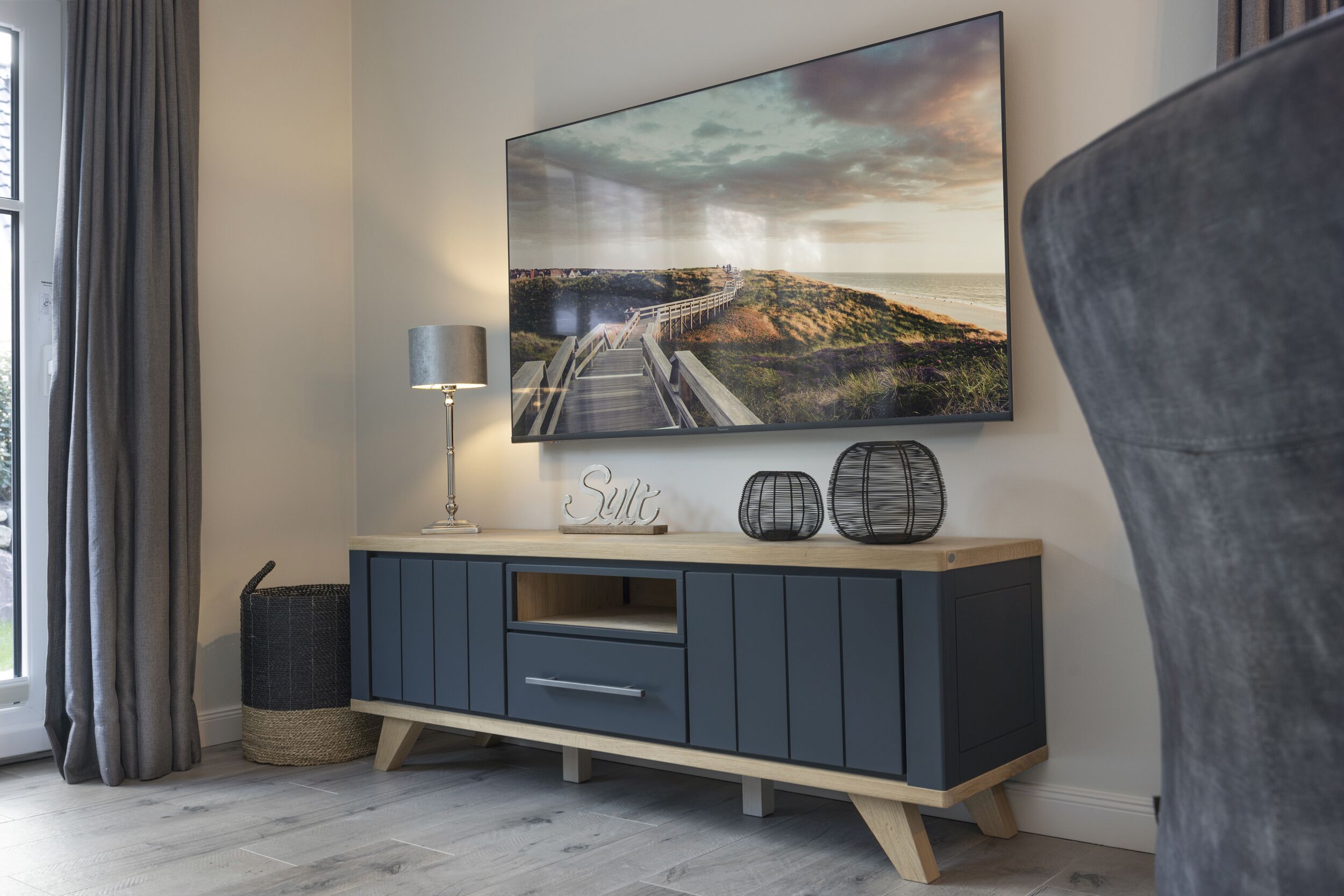 Un salon moderne doté d’un grand téléviseur à écran plat fixé au mur, d’un meuble de rangement gris foncé, d’une lampe et d’un élément décoratif.