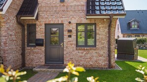 A brick house with a dark door, windows, and a small porch area. - House Munkmarscher Straße 14c (Westerland)