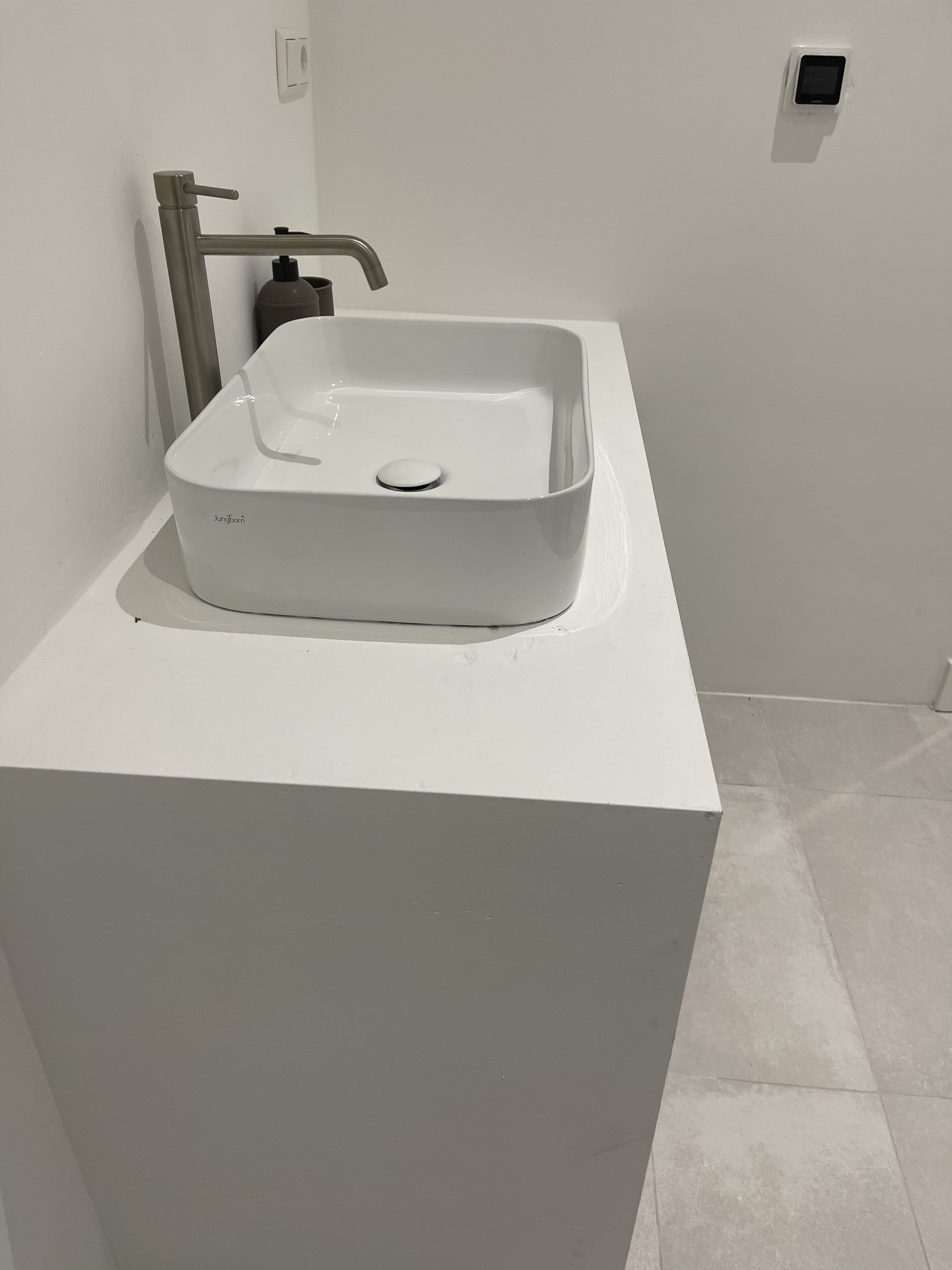 A modern bathroom with a white sink, a faucet, and a soap dispenser on a white countertop.