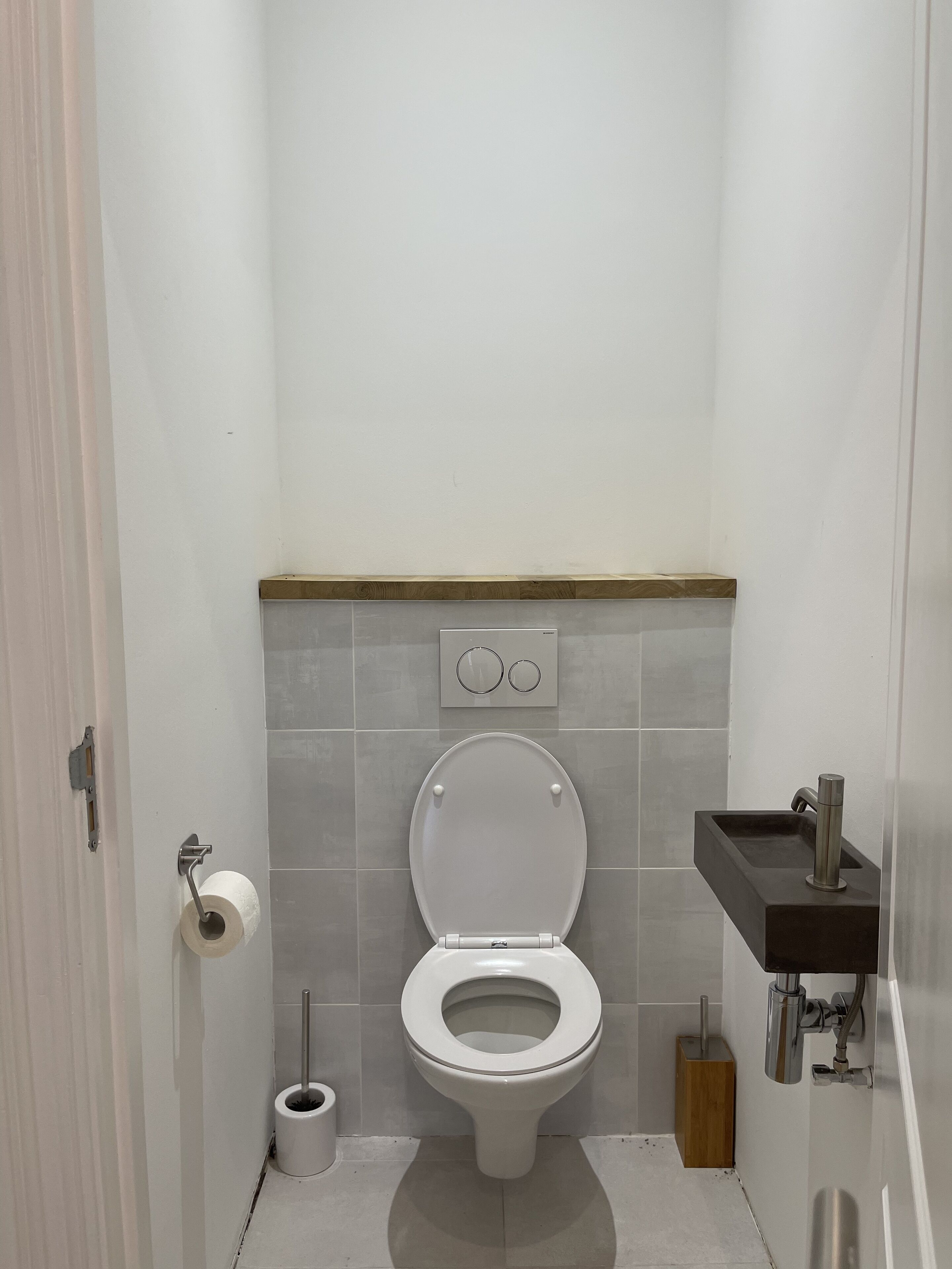 Een moderne badkamer met een toilet, toiletrolhouder, een douchetoilet en een wastafel met kraan.