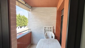 Un balcon avec une table et une chaise blanches, un mur en briques et une fenêtre donnant sur un espace verdoyant.