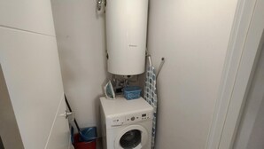 Une petite buanderie équipée d’un lave-linge, d’un chauffe-eau et d’un seau.