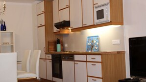Une cuisine compacte avec des meubles blancs, un four à micro-ondes, un lave-vaisselle et un téléviseur.