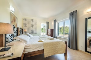 A bedroom with a bed, bedside table, lamp, and a view of the outdoors through a window.