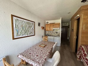 A compact room with a dining table, a map on the wall, a kitchenette, and a wooden door.