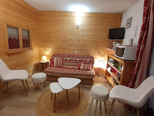 A cozy room with a wooden interior, a sofa, two chairs, a small table, a television, and a shelf with various items. - Spacious Studio Cabin for 4, Near Slopes and Village, Balcony, Free Ski Shuttle (Arêches-Beaufort)