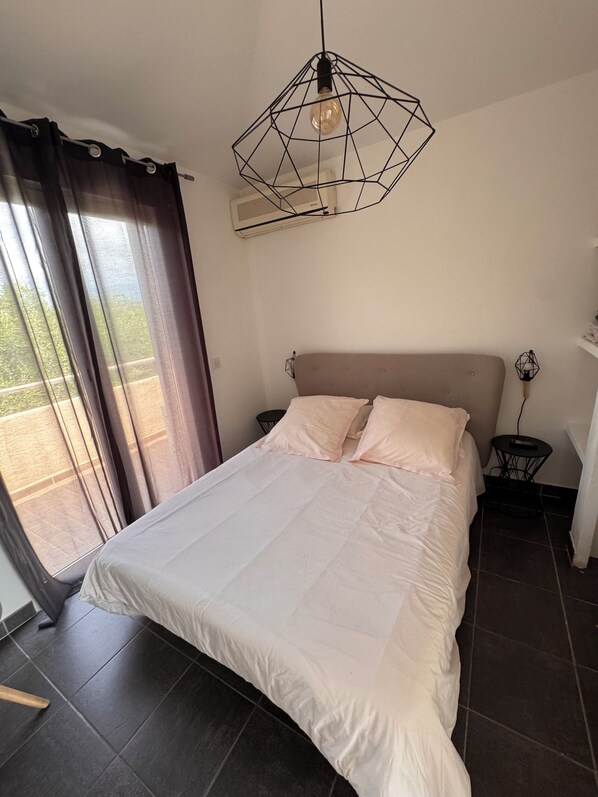 A bedroom with a bed, a geometric pendant light, a small table, and a window with curtains.