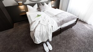 Una cama bien hecha con sábanas blancas y una manta gris, una lámpara de noche y una mesita con lámpara.