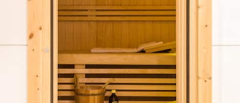 A wooden sauna with benches, a wooden bucket, and bottles of oils.