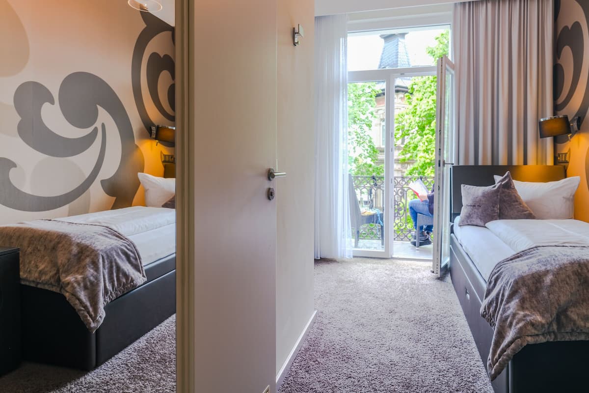 A hotel room with two beds, a large window with curtains, and a view of the outside.