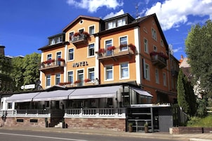 A multi-story hotel with balconies adorned with flowers, a covered outdoor seating area, and a sign indicating it includes a restaurant and lounge bar.