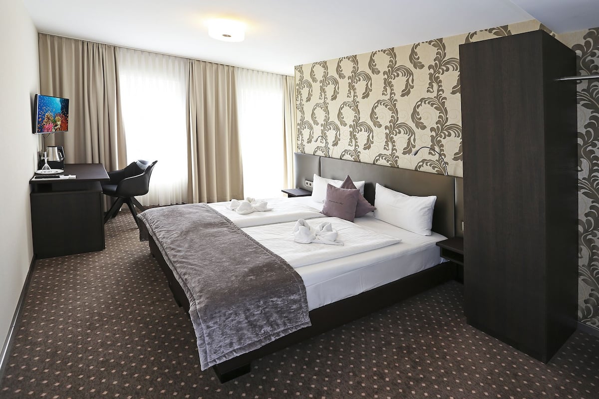 A hotel room with a large bed, a desk with a computer, and a TV.