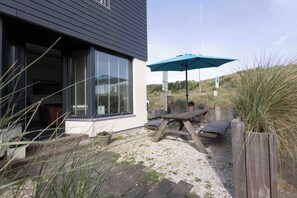 A modern house with a patio, a wooden table, and a blue umbrella. - Top location! Next to lighthouse, beach 50m FLOW (Egmond aan Zee)