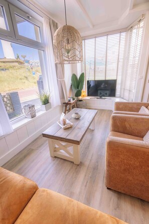 A living room with a wooden coffee table, a sofa, a television, and a large window with blinds.