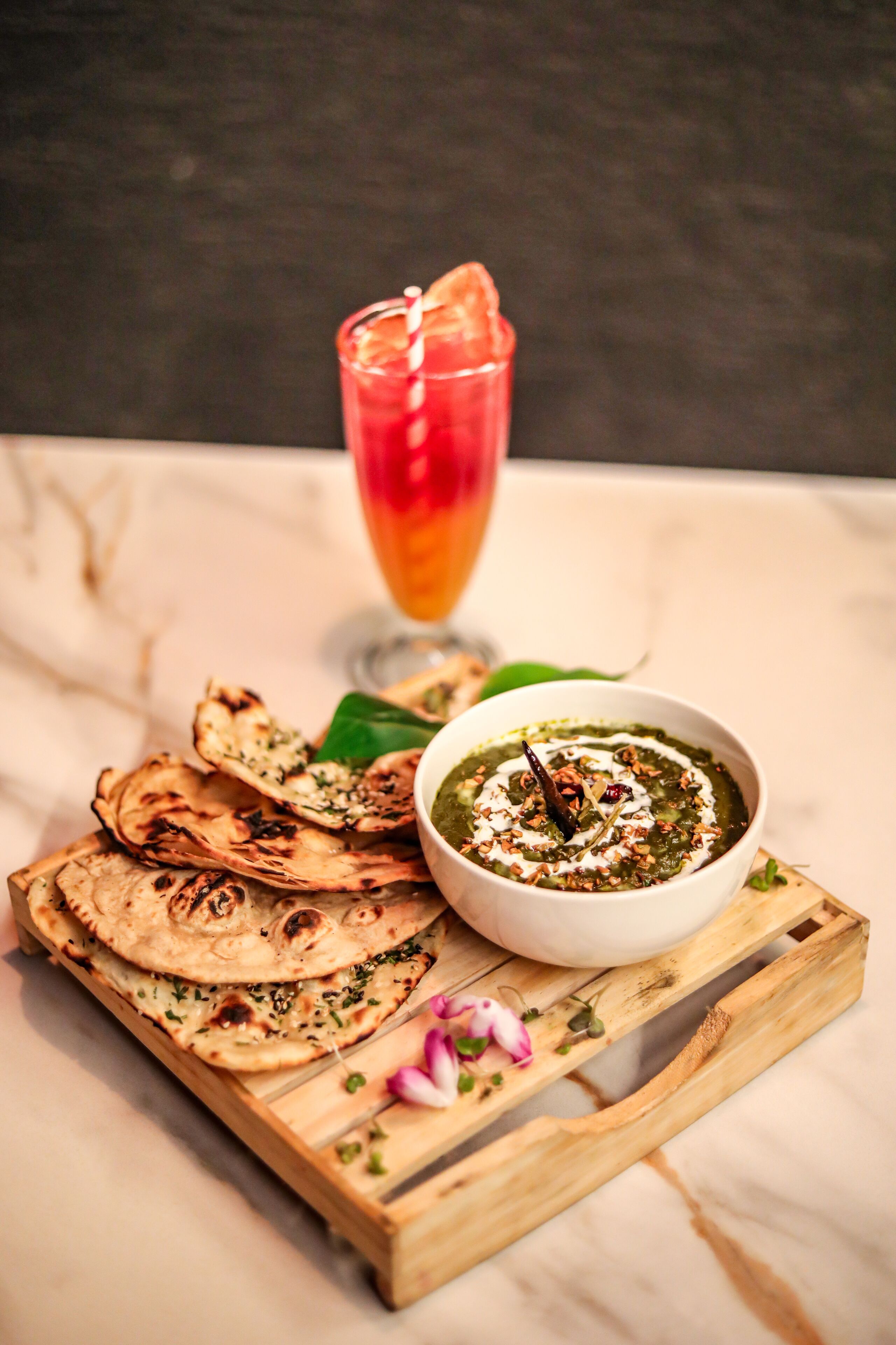 A wooden tray with flatbreads, a bowl of green dip, and a glass of red drink.