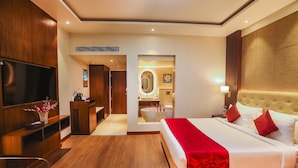 Habitación de hotel con una cama grande, televisión, escritorio y baño visible a través de una puerta abierta.