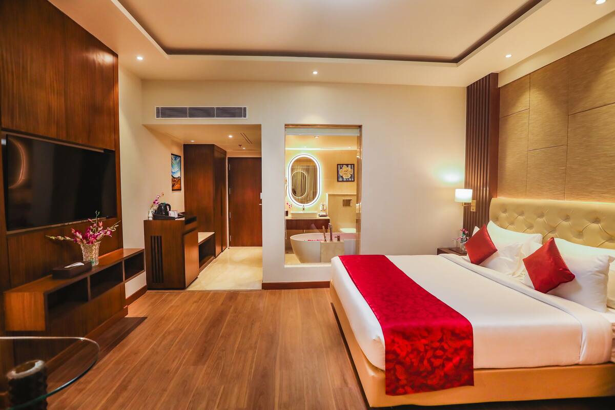 Une chambre d’hôtel avec un grand lit, une télévision, un bureau et une salle de bain visible à travers une porte ouverte.