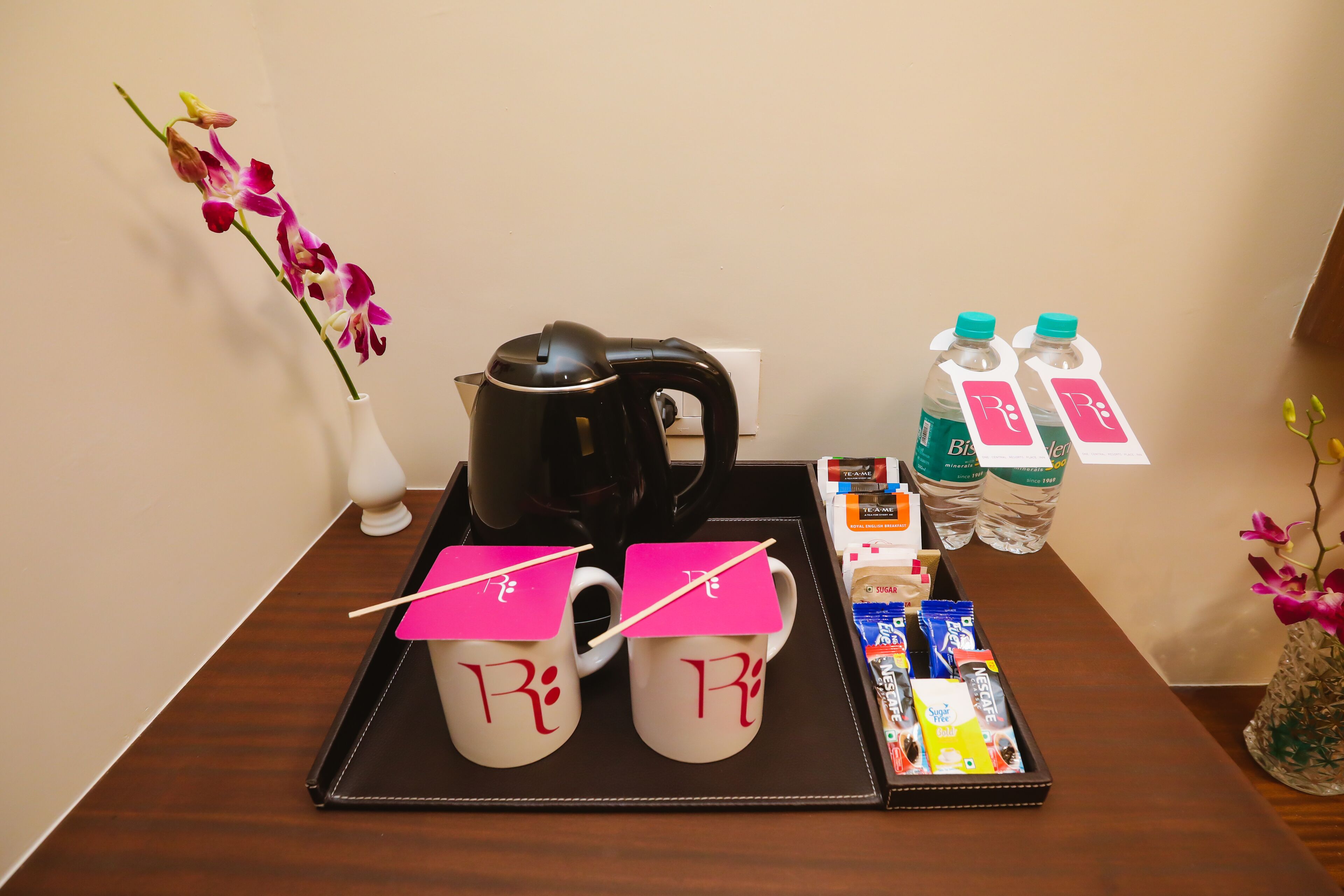 Una bandeja con dos tazas, un hervidor de agua, agua embotellada y aperitivos sobre una mesa de madera.