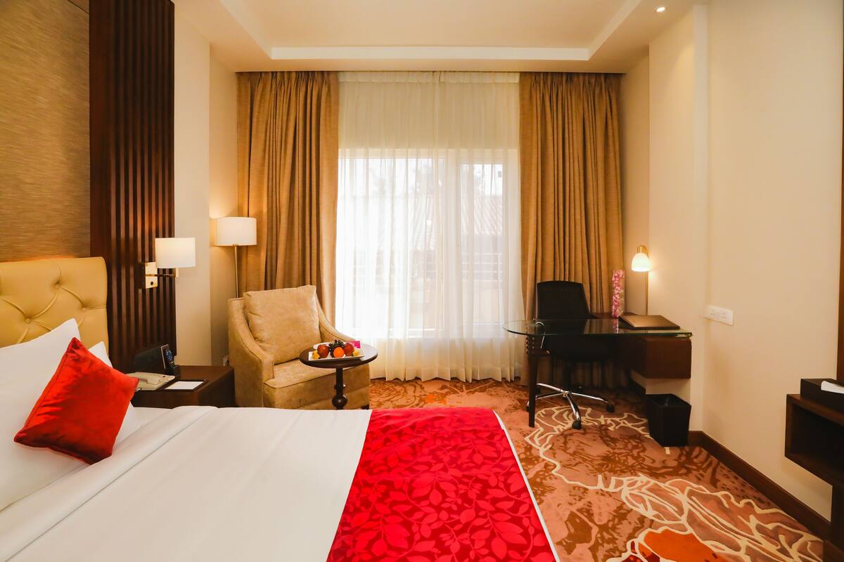 Une chambre d’hôtel avec un lit, une chaise, un bureau et une grande fenêtre avec des rideaux.