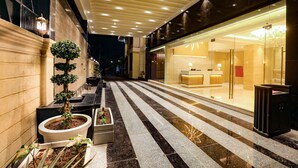Un pasillo de hotel con piso de mármol, plantas en macetas y una zona de recepción con puertas de cristal.