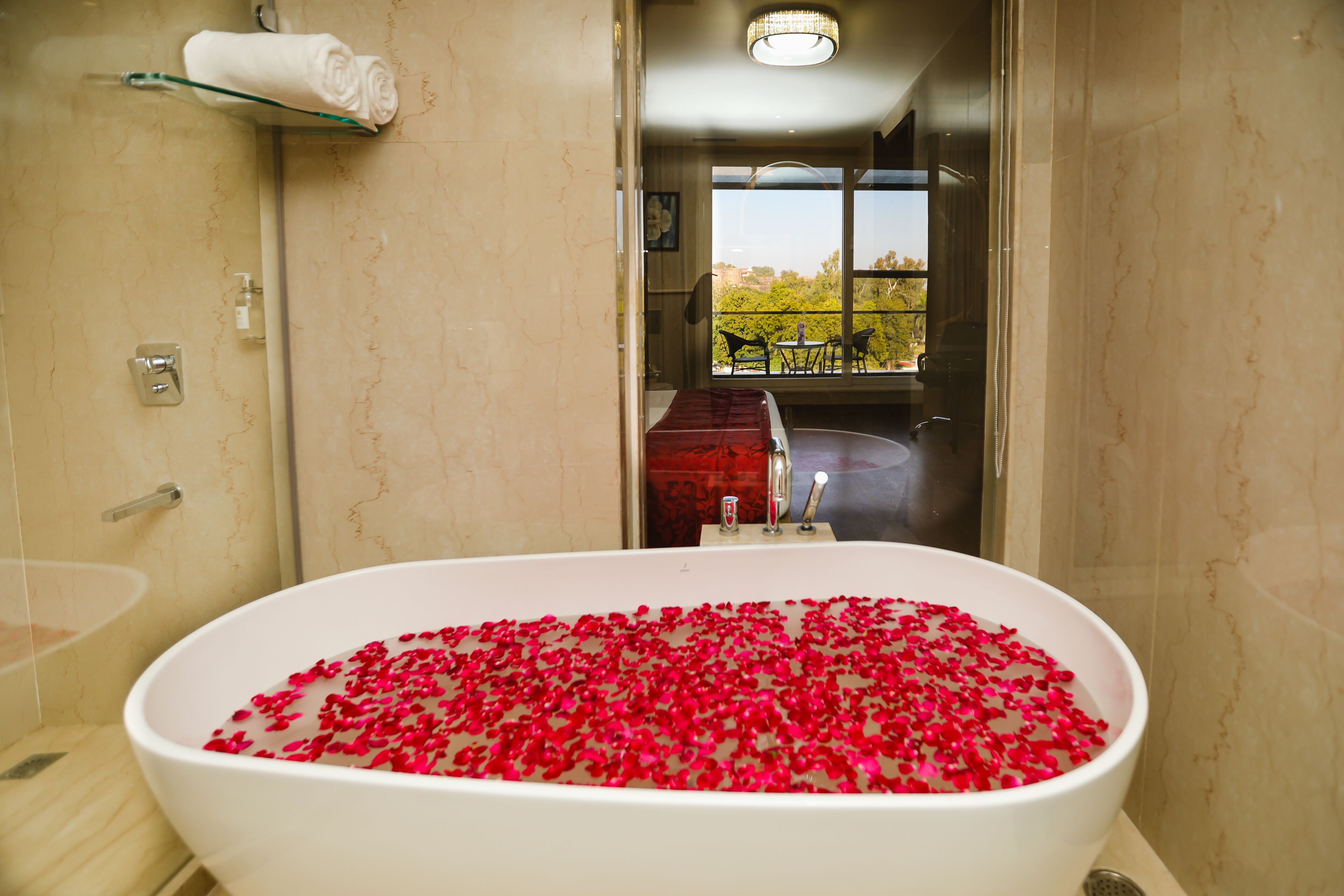 A bathroom with a bathtub filled with rose petals, a towel rack, and a window with a view.