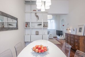 A modern living room with a dining area, white furniture, a television, and a decorative bird sculpture.