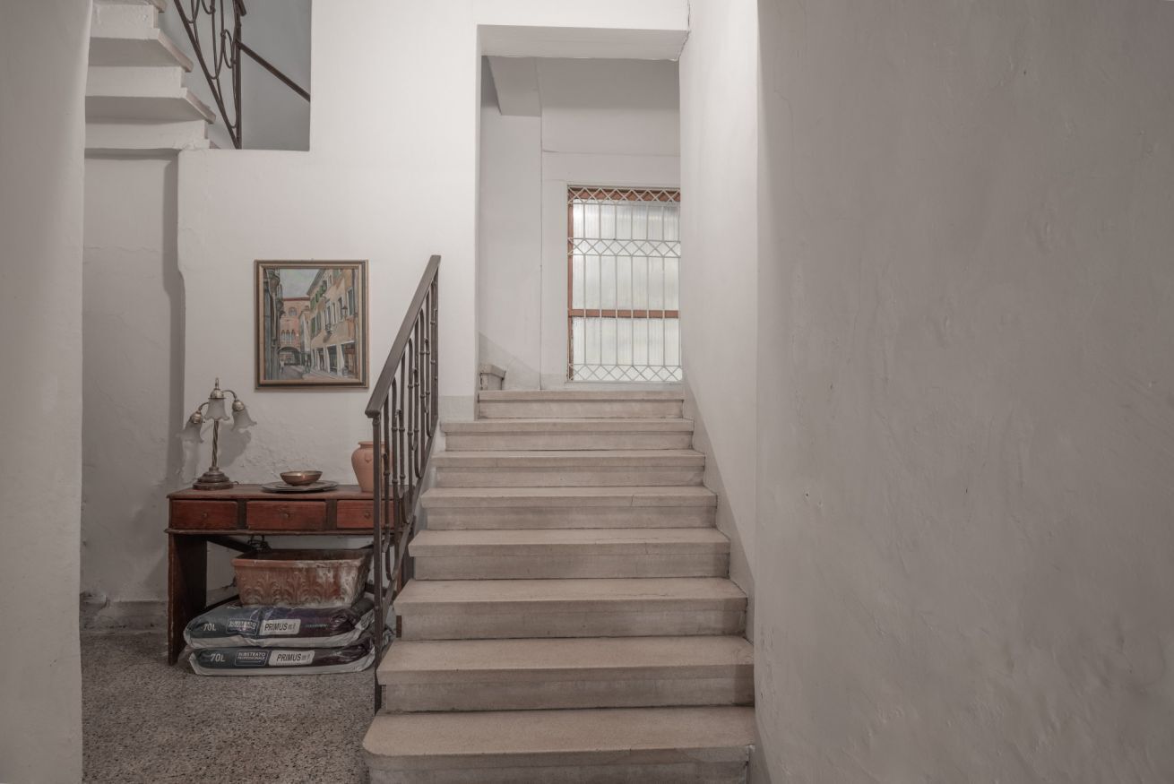 A staircase with a metal railing, a painting on the wall, and a window with metal bars.
