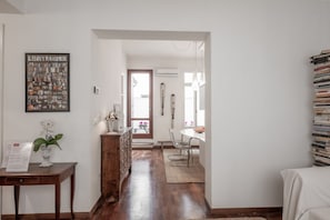 Un pasillo con piso de madera, un comedor con mesa y sillas, una estantería y un cuadro en la pared.