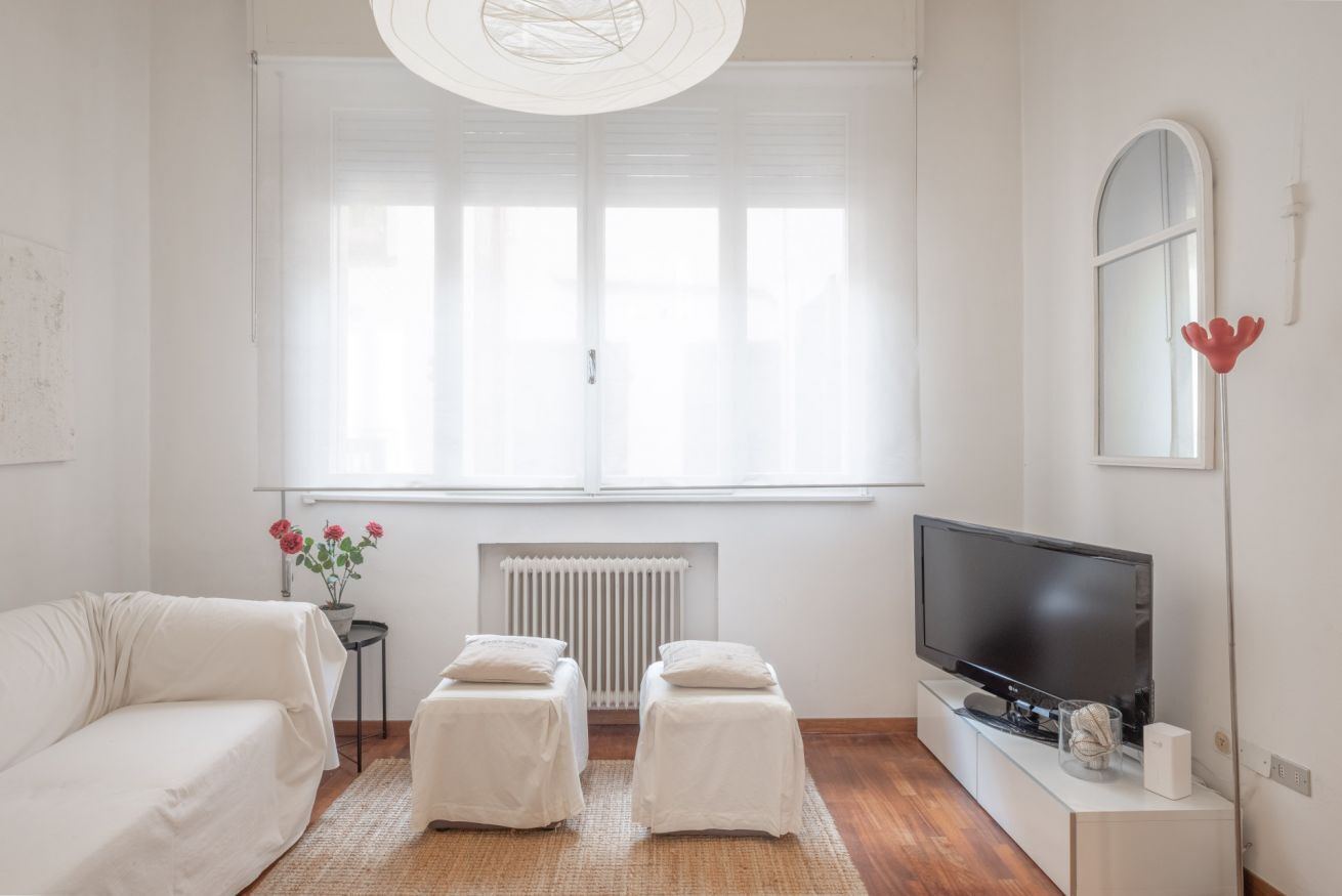 A modern living room with a sofa, two ottomans, a TV, and a radiator.