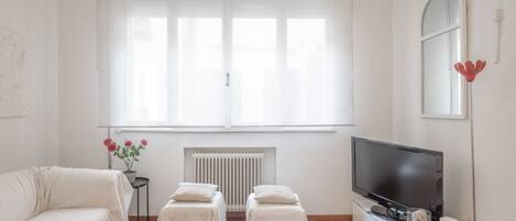 A modern living room with a sofa, two ottomans, a TV, and a radiator.