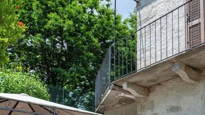 Ein Steinhaus mit einem Balkon, einer überdachten Terrasse mit Tisch und Stühlen und einer Steinsäule.