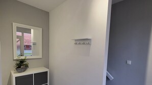 A hallway with a white console table, a mirror, and a small plant. There is a light switch on the wall and a staircase to the right. - Beautiful holiday home with hot tub. In short: relax and enjoy! (Neubörger)
