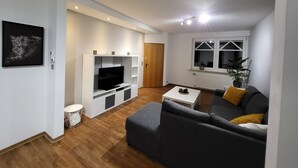 A modern living room with a grey sofa, a flat-screen TV, and a small white table. - Beautiful holiday home with hot tub. In short: relax and enjoy! (Neubörger)