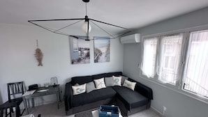 A modern living room with a black sectional sofa, a white coffee table, and a dining area with a small table and chairs. - Bright T3 Apartment Near Center - 3 Stars, Air Conditioning (Balaruc-les-Bains)