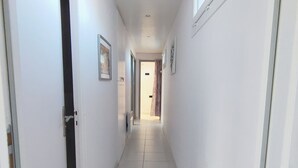 A narrow, tiled hallway with white walls and doors, leading to a room with a window and a door. - Bright T3 Apartment Near Center - 3 Stars, Air Conditioning (Balaruc-les-Bains)