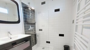 A modern bathroom with a glass shower enclosure, white tiles, and a black tiled accent wall. - Bright T3 Apartment Near Center - 3 Stars, Air Conditioning (Balaruc-les-Bains)