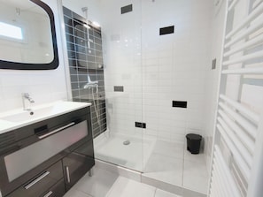 Une salle de bain moderne avec une douche à l’italienne en verre, des carreaux blancs et un mur d’accent recouvert de carreaux noirs.