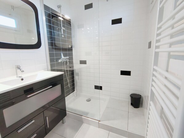 A modern bathroom with a glass shower enclosure, white tiles, and a black tiled accent wall.