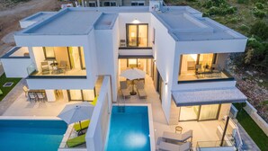 Et moderne hus med to etager, en swimmingpool, udendørs møbler og en balkon.