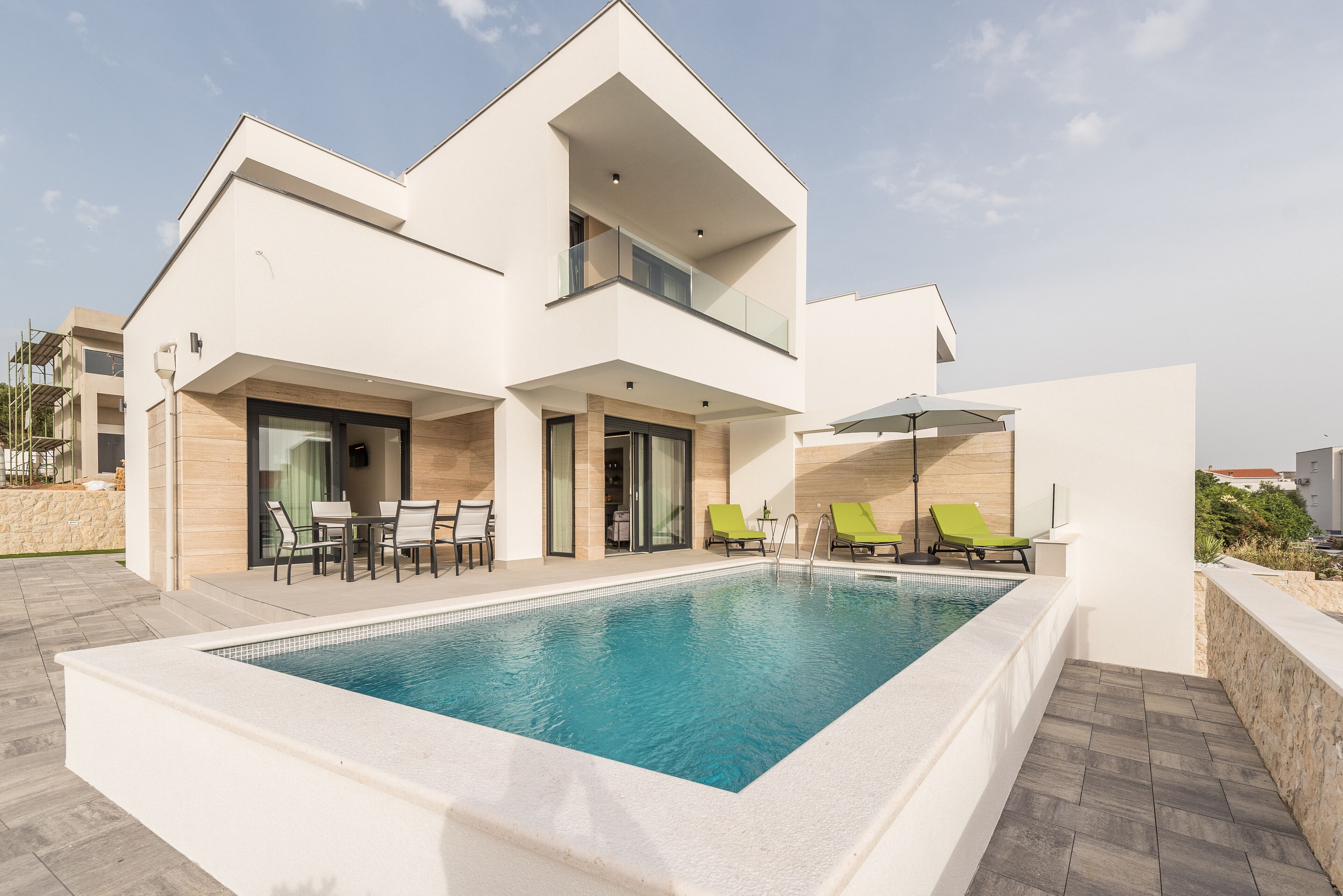 Ein modernes, zweistöckiges Haus mit Swimmingpool, Sitzgelegenheit im Freien und einem Balkon.