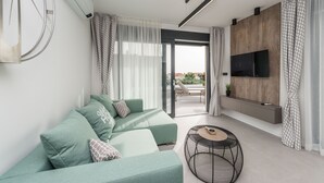 En moderne stue med en hjørnesofa, et fjernsyn monteret på en trævæg og en skydedør, der fører til et udendørs område.