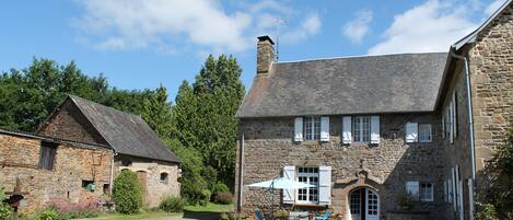 A stone building with a large front door, a chimney, and a small porch area with a table and chairs.