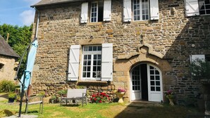 A stone building with white shutters, a bench, and potted plants.