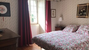 A bedroom with a bed, a nightstand, a lamp, a window with curtains, and a framed picture on the wall.