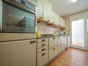 Cozinha equipada com forno embutido, micro-ondas e fogão a gás. Há armários com puxadores de madeira e painel de azulejos.