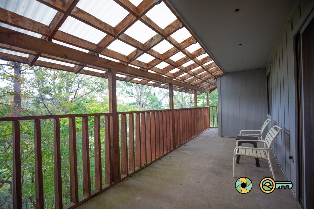 Un balcon abrité avec des balustrades en bois, un sol en béton et deux chaises en métal blanches.